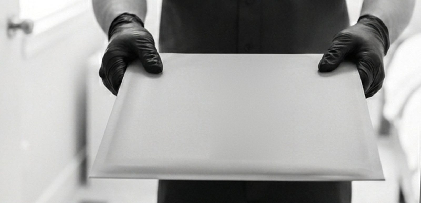 A flat letter, mailed in a white rigid mailer, held out with both hands